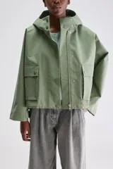Campera de calce relajado y silueta amplia color verde, con capucha integrada, cierre frontal con cremallera oculta por cartera de broches y bolsillos delanteros con solapa.
