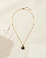 Collar de acero con baño de oro, compuesto por una cadena fina de eslabones y un dije circular con piedra central de color negro.