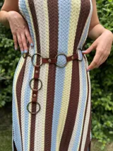 Cinturón de cuero marrón con múltiples aros metálicos de color bronce. El cinturón se ajusta mediante un gancho que se engancha en los aros.