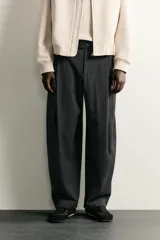 Pantalón de corte balloon fit en color gris oscuro, confeccionado en tejido con viscosa. Presenta pliegues frontales, cintura ajustable con cinturón integrado, bolsillos laterales y bolsillos traseros de doble vivo. Cierre frontal con cremallera y botón.