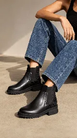 Bota tipo Chelsea de cuero negro, con paneles laterales elásticos y detalle de textura grabada en la parte trasera. Cuenta con suela track dentada y tirador en la parte superior.