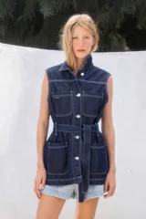 Chaleco de jean azul oscuro, con cuello camisero, cierre frontal de botones plateados, y bolsillos tipo parche en el pecho y la cadera. Incluye un cinturón de jean para ajustar la cintura.