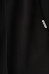 Pantalón tipo jogger negro, de corte recto y silueta clásica, confeccionado en tejido de punto de mezcla de algodón. Presenta pliegue cosido frontal, cintura elástica con cordón ajustable y bolsillos laterales y trasero insertado.