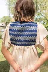 Túnica de lino color crudo con corte holgado y mangas cortas. Presenta una pechera cuadrada en el frente y la espalda confeccionada con textiles antiguos en color azul con patrones geométricos de ondas.
