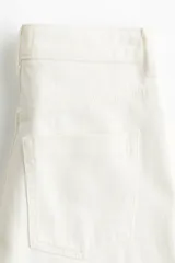 Jean amplio de tiro alto confeccionado en denim rígido color blanco, con diseño de cinco bolsillos y cierre frontal con botón y cremallera.