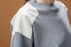 Sweater de punto color beige con cuello redondo y detalles de parches en cuero sintético blanco en los hombros. Presenta mangas largas con puños acanalados y un corte holgado.