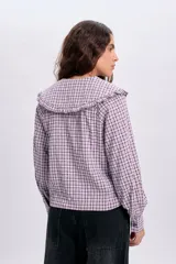 Camisa de manga larga con estampa a cuadros en tonos violeta y blanco, con cuello babero amplio con volados y cierre frontal abotonado.