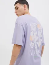 Camiseta lila de manga corta con estampado en la espalda de hojas y círculos en tonos blanco y naranja.