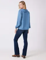 Blusa de lyocell color azul claro, con escote en V y volados en el cuello y la parte frontal. Tiene mangas largas con puños elásticos y cierre de botones en la parte delantera.