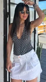 Top halter negro con estampado de lunares blancos, escote pronunciado en V y ajuste en la espalda.