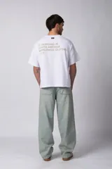 Remera de corte boxy y fit cuadrado, confeccionada en algodón grueso de alta calidad. Presenta un diseño minimalista en el frente con un pequeño logo circular y una estampa de gran tamaño en la espalda con la frase 'Designed in South America, Worldwide Clothes'.