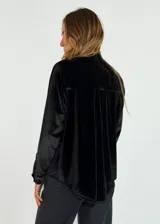 Camisa de terciopelo color bordó, con cuello mao y cierre frontal de botones. Presenta detalles de volados verticales a ambos lados de la botonera y mangas largas con puños abotonados.