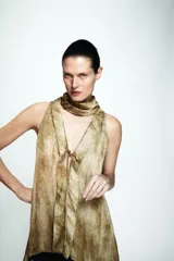 Top sin mangas con cuello tipo choker y escote en pico con lazada frontal. Presenta un diseño con efecto tie-dye en tonos tierra y cierre posterior con abertura y botón.