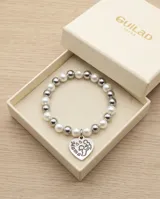 Pulsera elástica compuesta por una combinación de perlas blancas y esferas metálicas plateadas, con un dije colgante en forma de corazón con grabado.