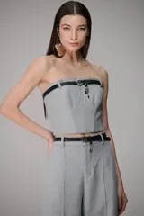 Top tipo corset strapless de color gris, con diseño estructurado y detalle de pasante de cuero negro en la parte superior. Presenta un calce ajustado que realza la silueta.