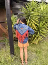 Camisa de jean con diseño estilo western, featuring un canesú trasero con estampado paisley en blanco y azul, y flecos largos de cuero rojo. Cuenta con mangas largas abullonadas con puños elásticos fruncidos.