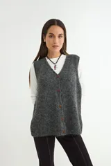 Chaleco tejido de punto en color gris oscuro, con escote en V y cierre frontal de botones marrones. Presenta una textura suave y un corte holgado.