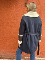 Saco de paño azul marino con solapas amplias y puños en corderito sintético color crema. Presenta detalles en cuero sintético marrón en la parte frontal y en las mangas, con un diseño abierto y corte recto.