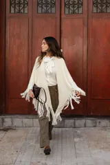 Poncho triangular de lana en color crudo, con diseño de tejido texturizado y terminaciones de flecos largos en todo el borde.