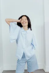 Camisa de lino color tostado, con cuello camisero y cierre frontal de botones. Se caracteriza por sus mangas cortas amplias y voluminosas que aportan un diseño fresco y liviano.