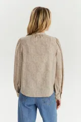 Blusa de manga larga con diseño de hombros abullonados y cuello redondo pequeño. Presenta cierre frontal con botones y un estampado fino de puntos sobre fondo beige.