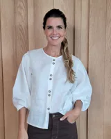 Camisa de lino color blanco, con cuello redondo, cierre frontal con botones y mangas abullonadas con puños elásticos.