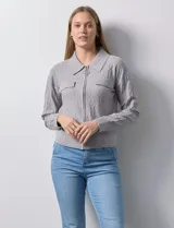 Cardigan de tejido jacquard color gris con diseño geométrico en relieve. Presenta cuello con solapa, cierre frontal completo y bolsillos decorativos en el pecho.