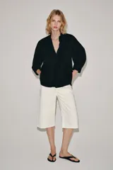 Camisa de cuello redondo y manga corta abullonada, color negro, de corte recto con aberturas laterales y cierre frontal con botones. Perteneciente a la colección ZARA Woman Collection.