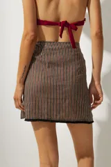 Falda corta tipo pareo con diseño envolvente, confeccionada en tela con estampado de rayas verticales en tonos tierra. Cuenta con un lazo lateral para ajuste y un borde inferior con detalle de costura en contraste.