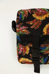 Mini bolso bandolera de poliéster color negro con estampado colorido de bananas. Cuenta con correa ajustable, solapa con cierre de hebilla plástica y detalles en red.