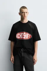 Camiseta negra de corte boxy fit con paneles laterales y de hombros en tejido de malla. Presenta un estampado frontal ovalado con borde rojo y texto blanco que dice "ECHO SHIFT".