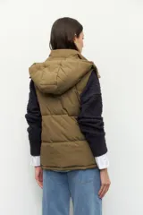 Chaleco puffer acolchado color verde oliva, con cuello alto, capucha desmontable y cierre frontal. Cuenta con bolsillos laterales funcionales.