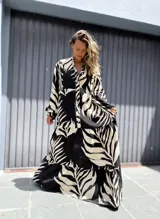 Vestido largo tipo túnica con estampado de hojas en contraste blanco y negro. Presenta cuello camisero con botones, mangas largas amplias y falda con volados escalonados.