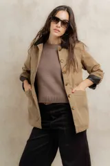 Campera color beige con cuello de corderito negro, cierre frontal con botones y forro interior. Presenta un diseño de corte recto y mangas largas con puños vueltos.