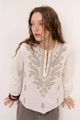 Blusa celeste de manga larga con delicados bordados florales en tono más claro en la zona del pecho y mangas. Presenta escote en V y puños elásticos abotonados.