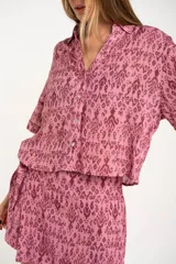 Camisa de manga corta con estampado abstracto en tonos rosa y borgoña. Tiene cuello camisero, cierre frontal con botones y corte oversize.