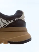 Championes urbanos de diseño exclusivo con paneles en cuero negro y textil estampado con motivo animal print de puntos. Presenta una suela de plataforma en tono marrón con relieve dentado y detalles en cuero beige en el talón.