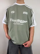 Remera de calce oversize estilo deportivo, color verde militar con mangas cortas blancas y detalles de franjas y estampas tipográficas en el frente.
