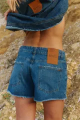 Short de jean azul con diseño de cinco bolsillos, tiro medio y bordes deshilachados. Cuenta con una etiqueta de cuero sintético en la parte trasera y avíos metálicos personalizados de la marca Renée.