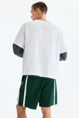 Short deportivo de color verde oscuro, confeccionado en nylon, con bandas laterales blancas, cintura elástica ajustable mediante cordón blanco y corte estándar.