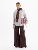 Camisa de poplín con diseño de rayas verticales en tonos azul y blanco. Presenta un cuello prolongado que se anuda en forma de lazo frontal, mangas largas con puños anchos y corte holgado.