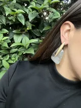 Aros colgantes con base de resina color violeta con detalles en negro y pieza metálica dorada opaca en forma de lanza.