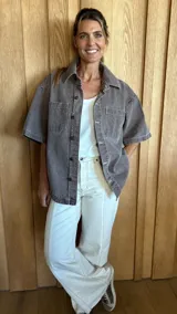 Sobrecamisa de denim soft en tono azul medio, con corte oversize, mangas cortas, cuello clásico y cierre frontal con botones metálicos. Presenta dos bolsillos frontales con solapa y un ruedo redondeado.