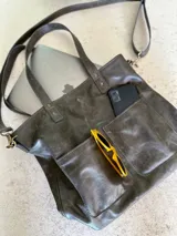 Cartera tipo tote bag color gris grafito, con doble asa de mano y correa bandolera extraíble y ajustable. Incluye dos bolsillos externos grandes.