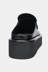 Mocasín destalonado de estilo mule, color negro, con diseño de antifaz y suela de plataforma dentada tipo chunky.