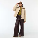 Campera de efecto borreguito en color beige, con cuello amplio y cierre frontal de botones negros. Presenta ribetes negros en contraste en el cuello, la apertura frontal y los puños. Marca Kiabi.