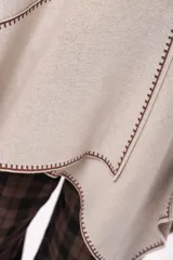 Ruana de algodón en color beige con detalles de costura decorativa en contraste color marrón. Presenta un diseño abierto con caída fluida y mangas tipo capa.