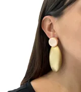Aros colgantes con forma geométrica, con un círculo pequeño color crema en la parte superior y una forma ovalada grande color dorado en la parte inferior.