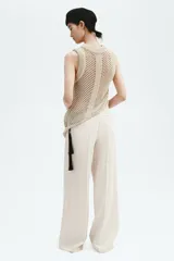 Pantalón sastrero de tiro alto en color beige, con perneras amplias y raya marcada en la parte delantera y trasera. Cuenta con cierre de cremallera, botón oculto y corchete, además de bolsillos decorativos insertados.