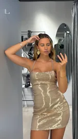Vestido corto dorado con lentejuelas, breteles finos y espalda descubierta.